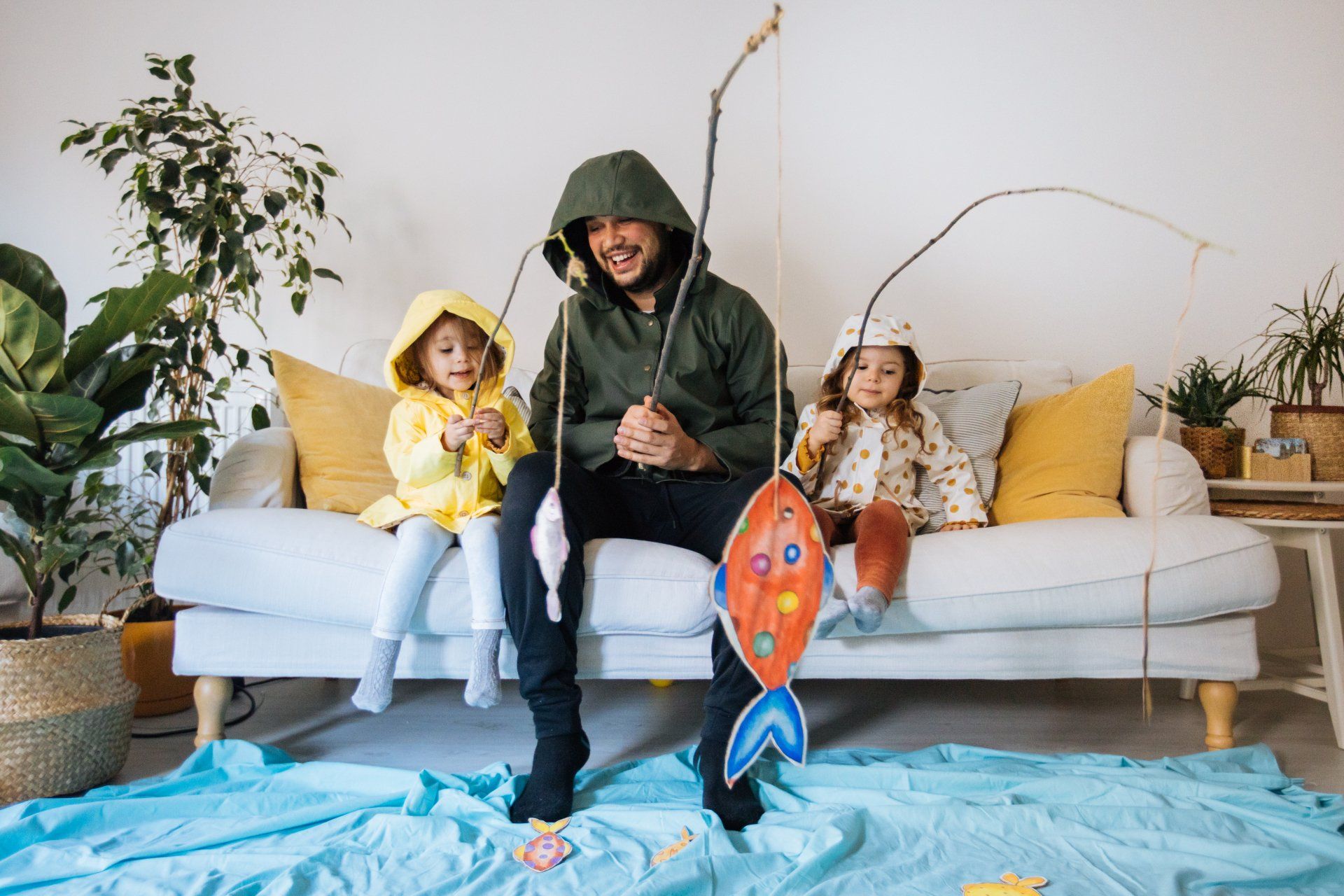 A man and two children are sitting on a couch holding fishing rods.