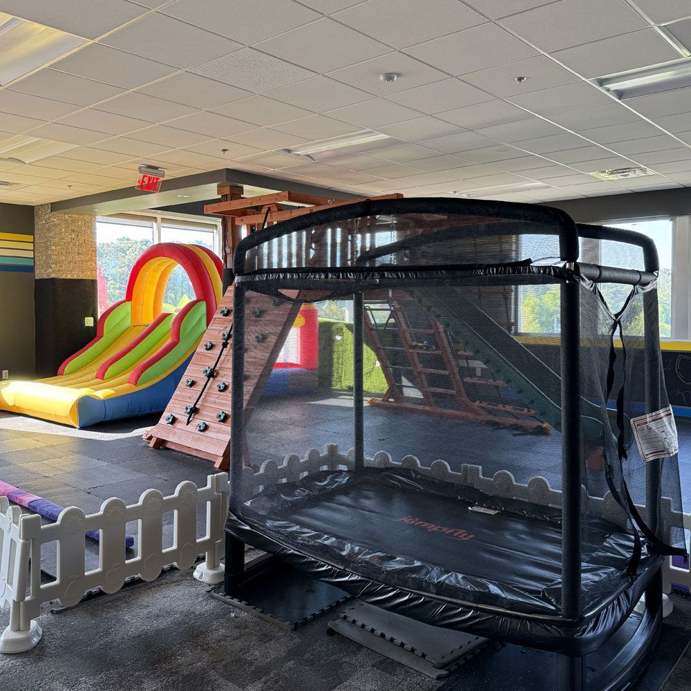 A large room with a trampoline , slide , and climbing wall.