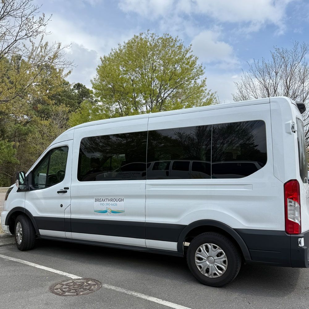 A white van is parked in a parking lot with trees in the background.