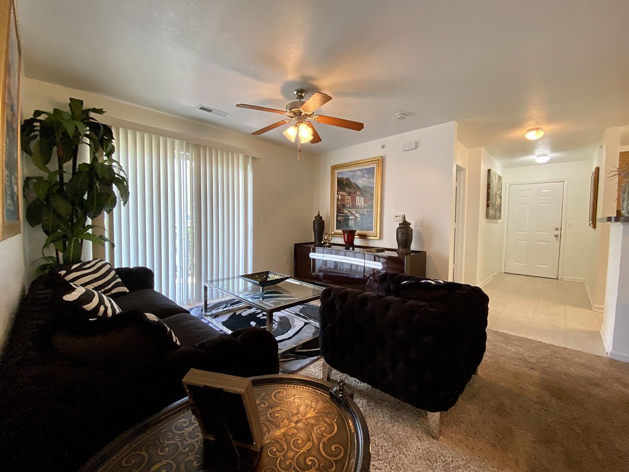 Living room with black furniture, glass table, tan carpet, and a hallway.