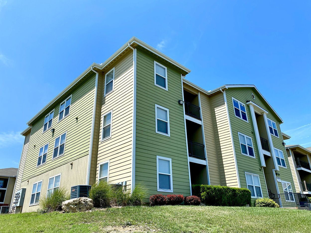 Apartment building with green and tan siding against a blue sky.