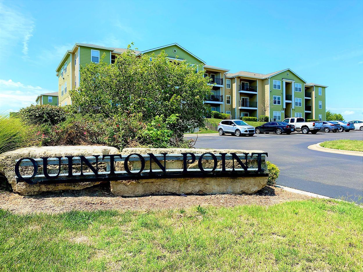 Sign for Quinton Point apartment complex with buildings and parked cars in background.