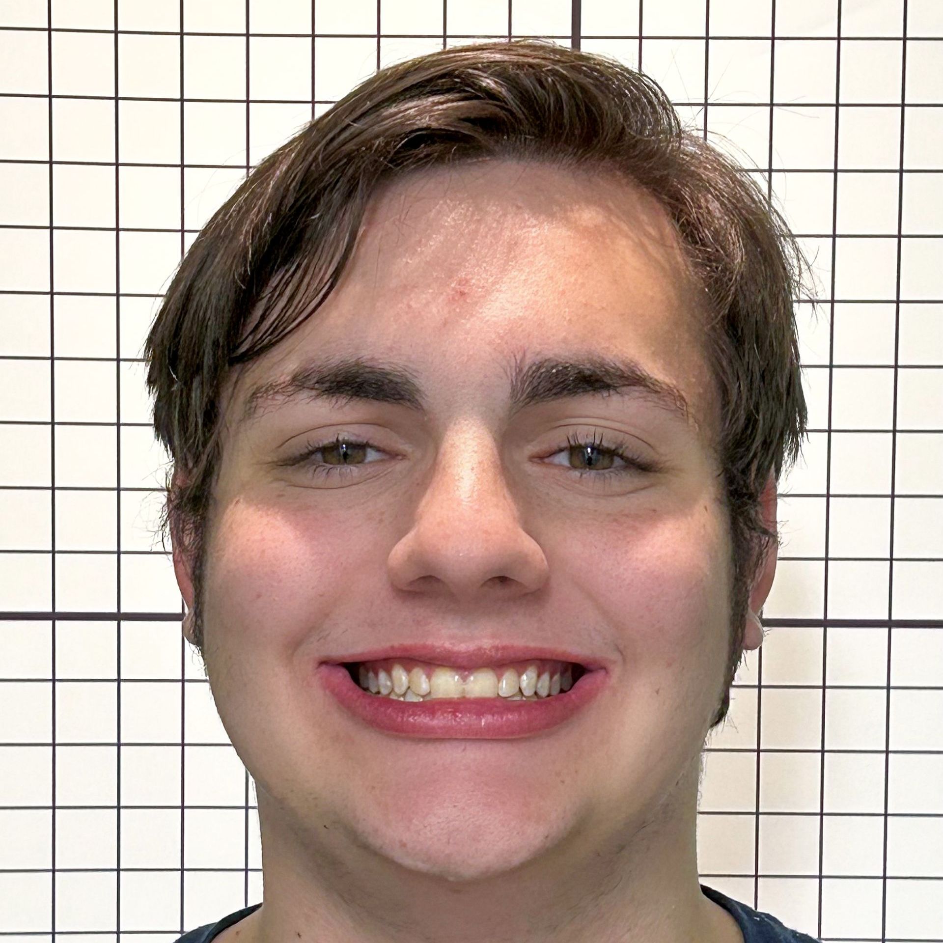 A young man is smiling for the camera in front of a white grid.