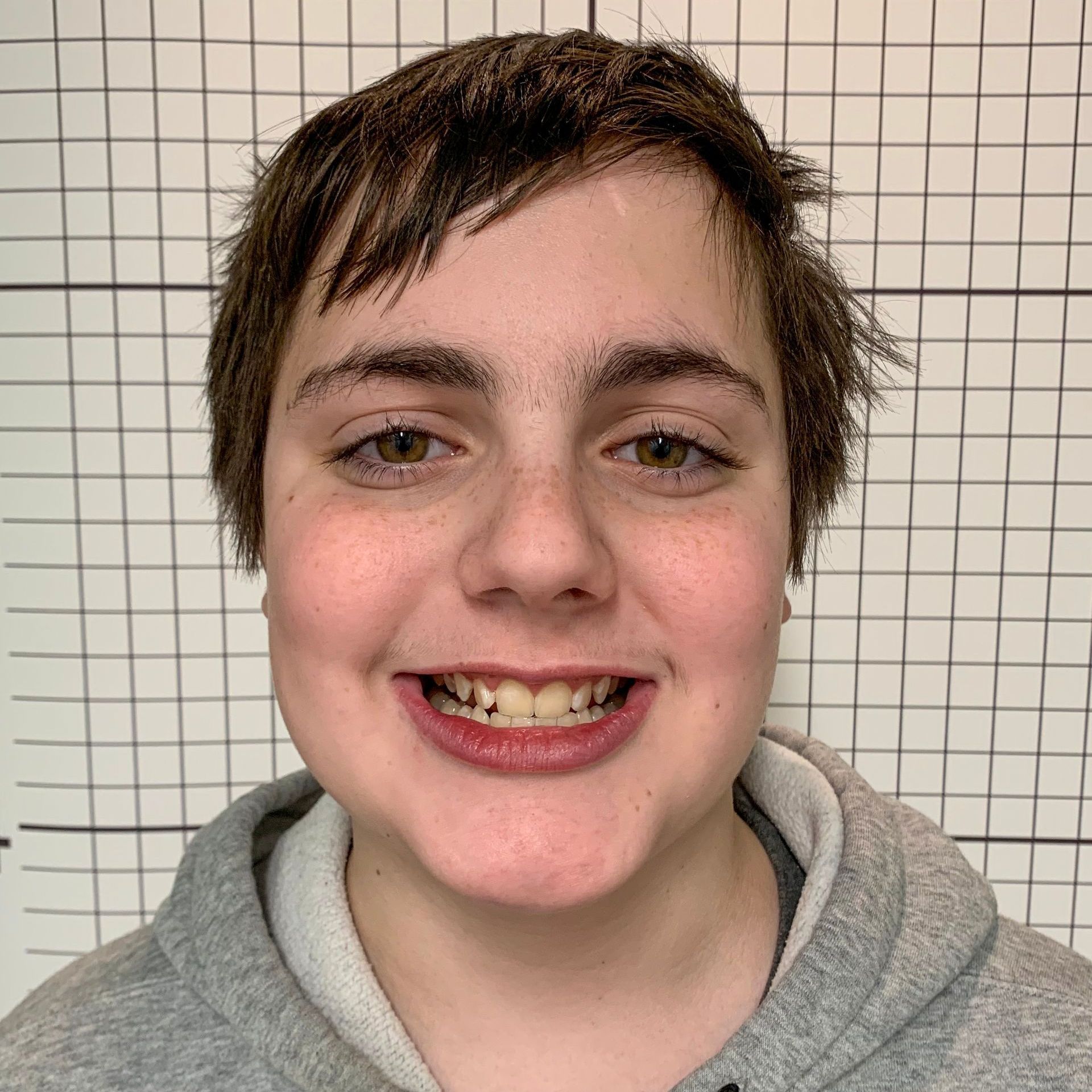A young man wearing a grey hoodie is smiling for the camera.