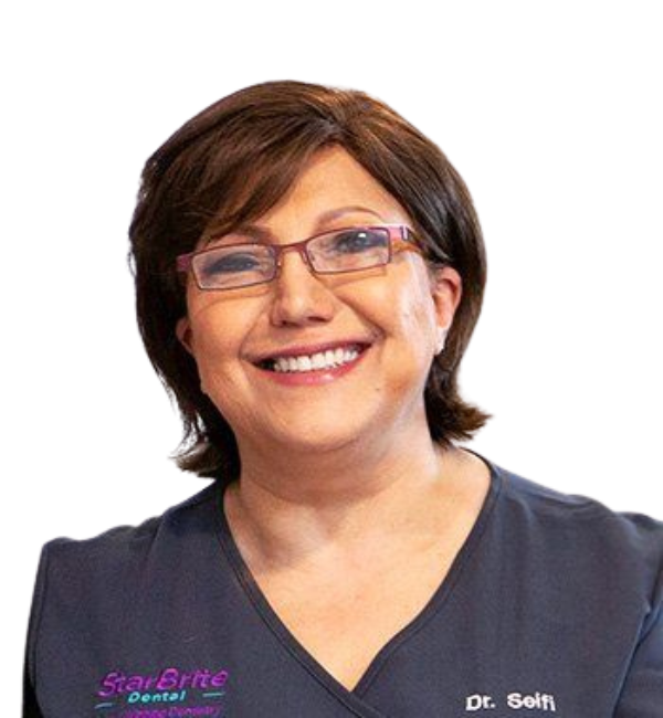 A woman wearing glasses and a scrub top is smiling.