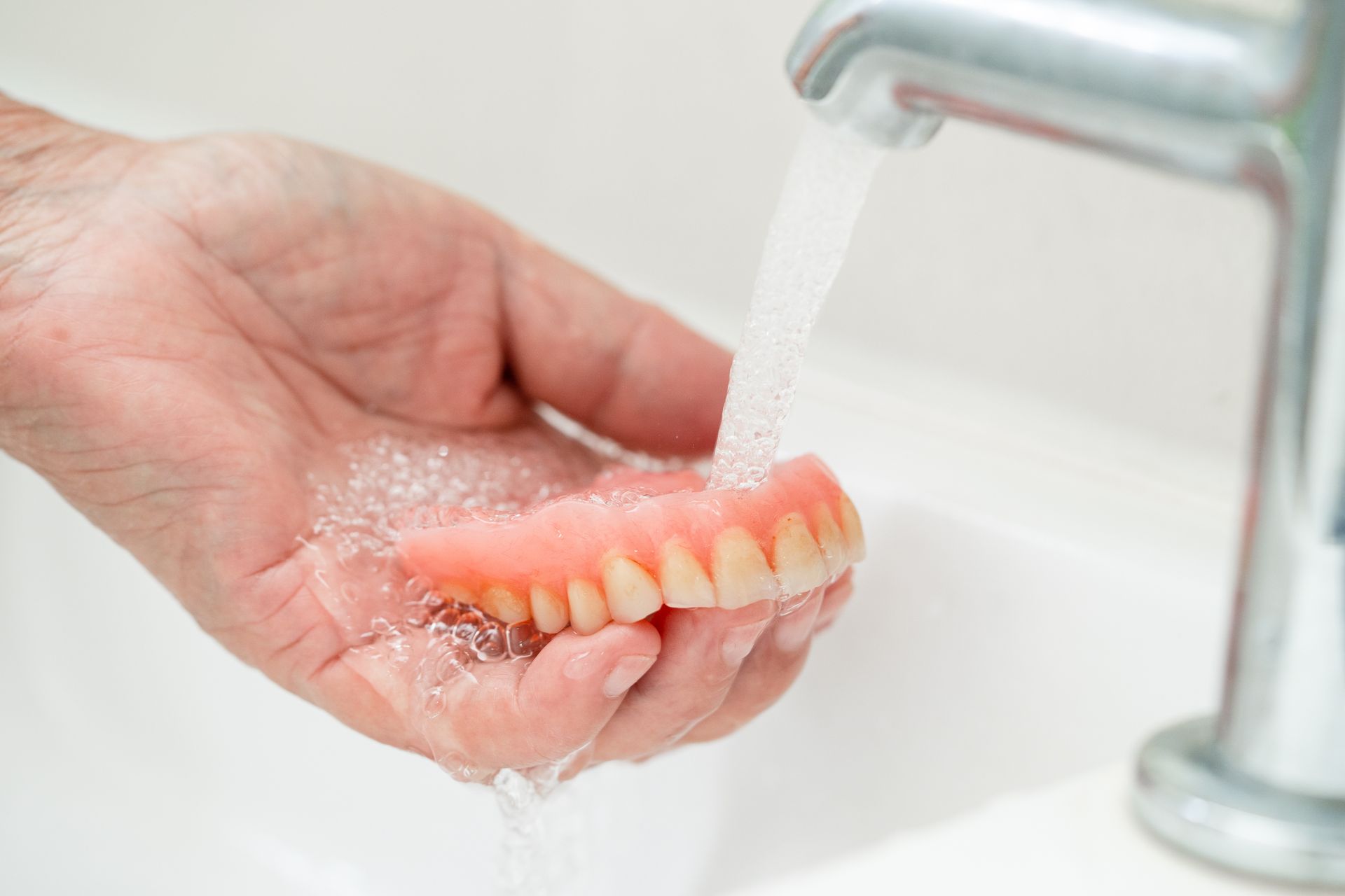 A person is washing a denture in a sink.