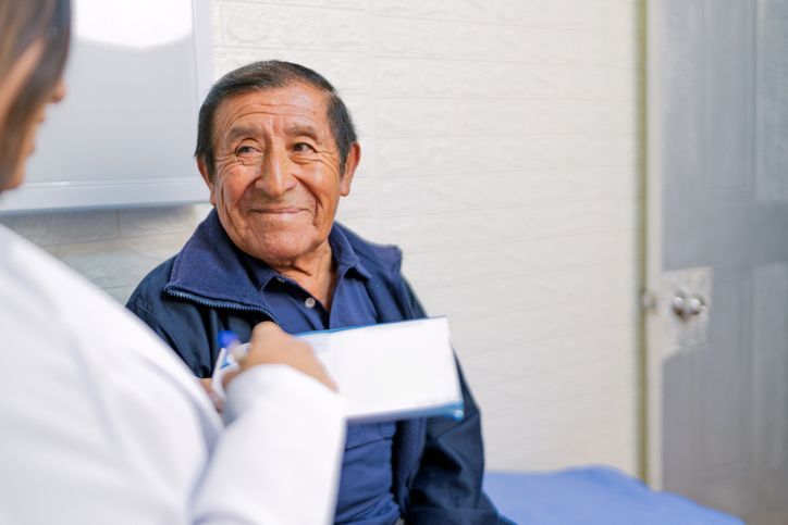 Dentist in blue gloves examining an elderly patient's mouth in a dental office. The patient smiles.