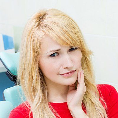 A woman is sitting in a dental chair with her hand on her face.