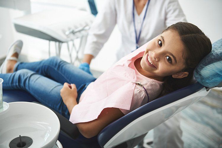 A little girl is sitting in a dental chair and smiling.