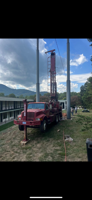 Red truck with a drilling rig beside a building and grassy field under a blue sky