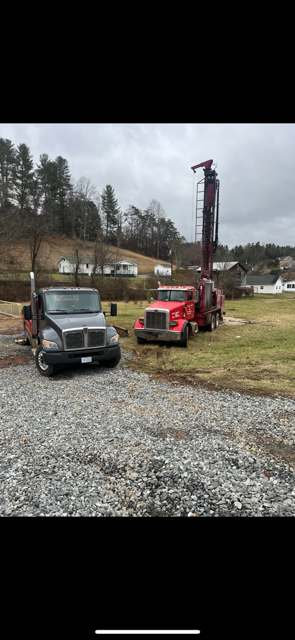 Red tow truck lifting a black car in a gravel lot with trees and houses nearby.