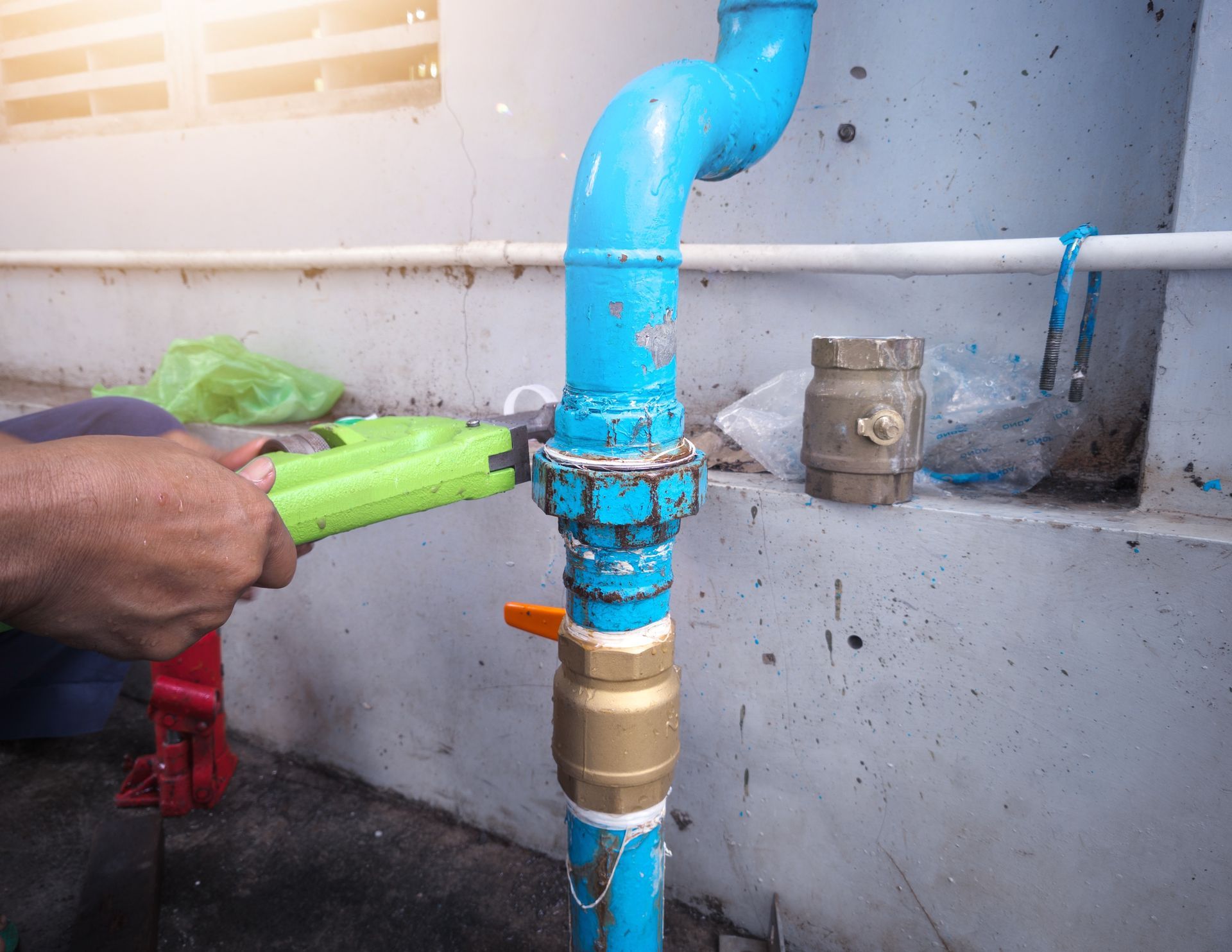 Plumber tightening a blue water pipe fitting with a large wrench during plumbing repair work.