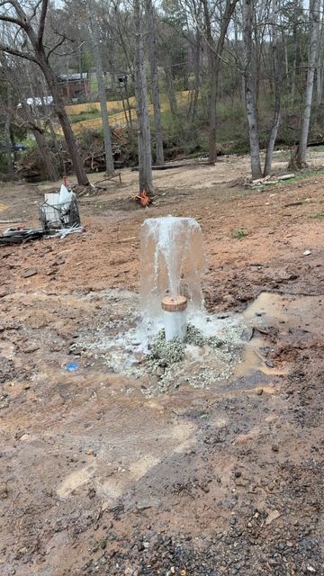 Small outdoor fire hydrant venting water in a wooded, muddy area near a road
