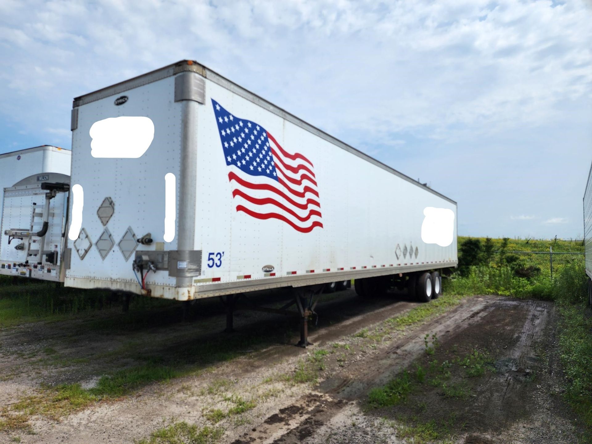 White semi-trailer with American flag painted on side, parked outdoors on a dirt lot.