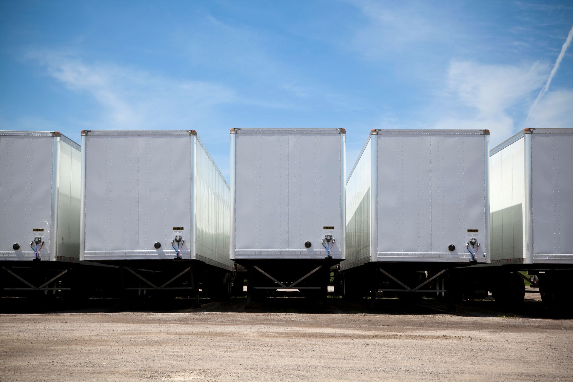 Row of white semi truck trailers parked on a lot under a blue sky. Row of white semi truck trailers parked on a lot under a blue sky.