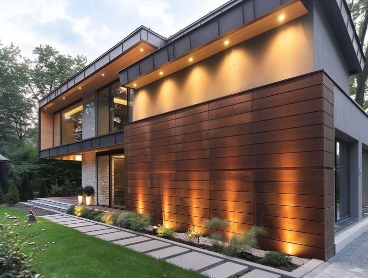 Modern two-story house with warm exterior lighting, wood siding, and a landscaped front path at dusk