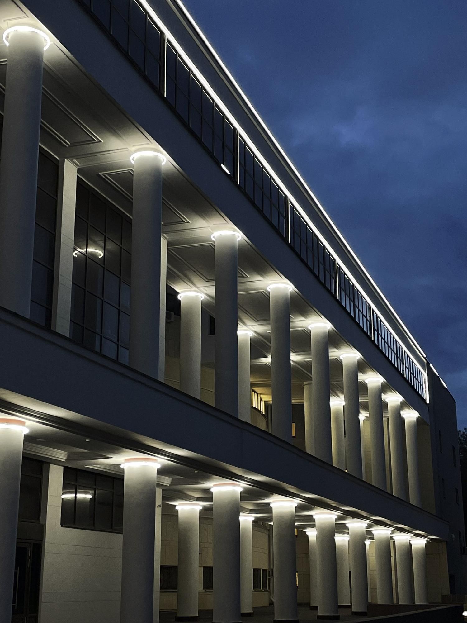 Modern building exterior at dusk with illuminated columns and windows against a blue sky