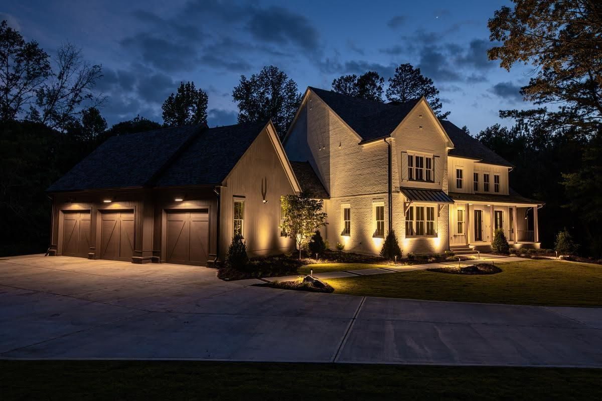 Large house with lit exterior lights and garage at dusk under a dark blue sky