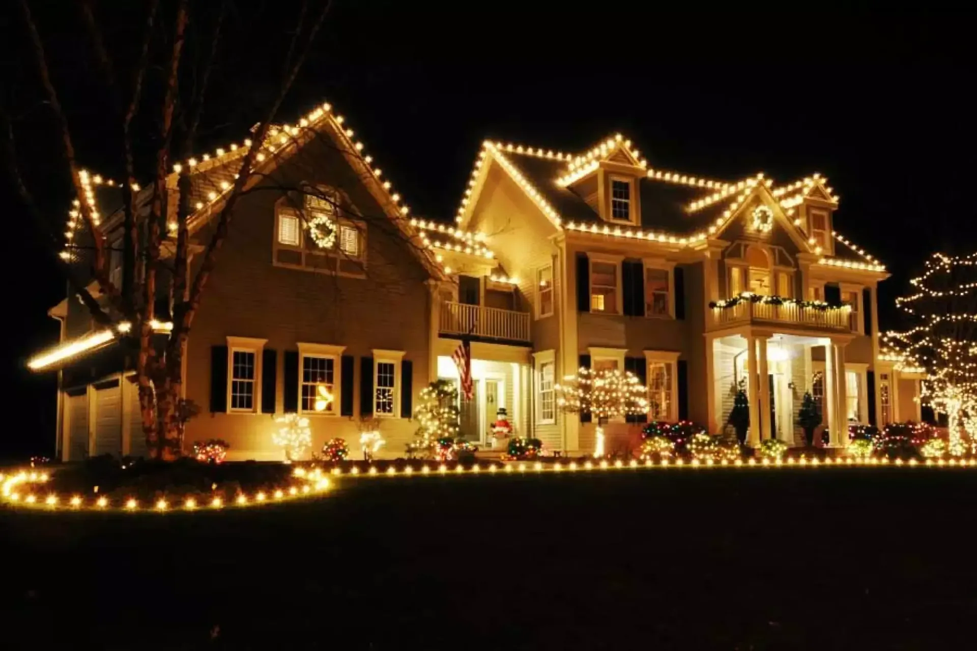 House decorated with warm white Christmas lights at night, glowing against a dark yard.