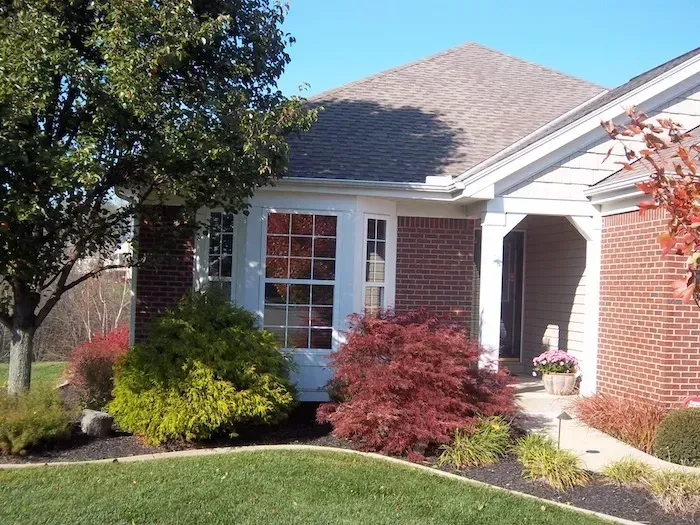 Brick house with white trim, front porch, and landscaped shrubs in a sunny yard