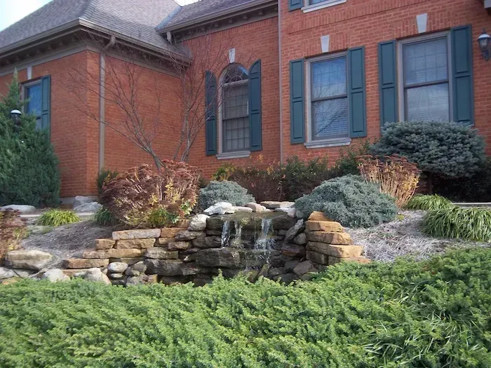 Brick house with blue shutters and a stone garden wall amid shrubs and greenery