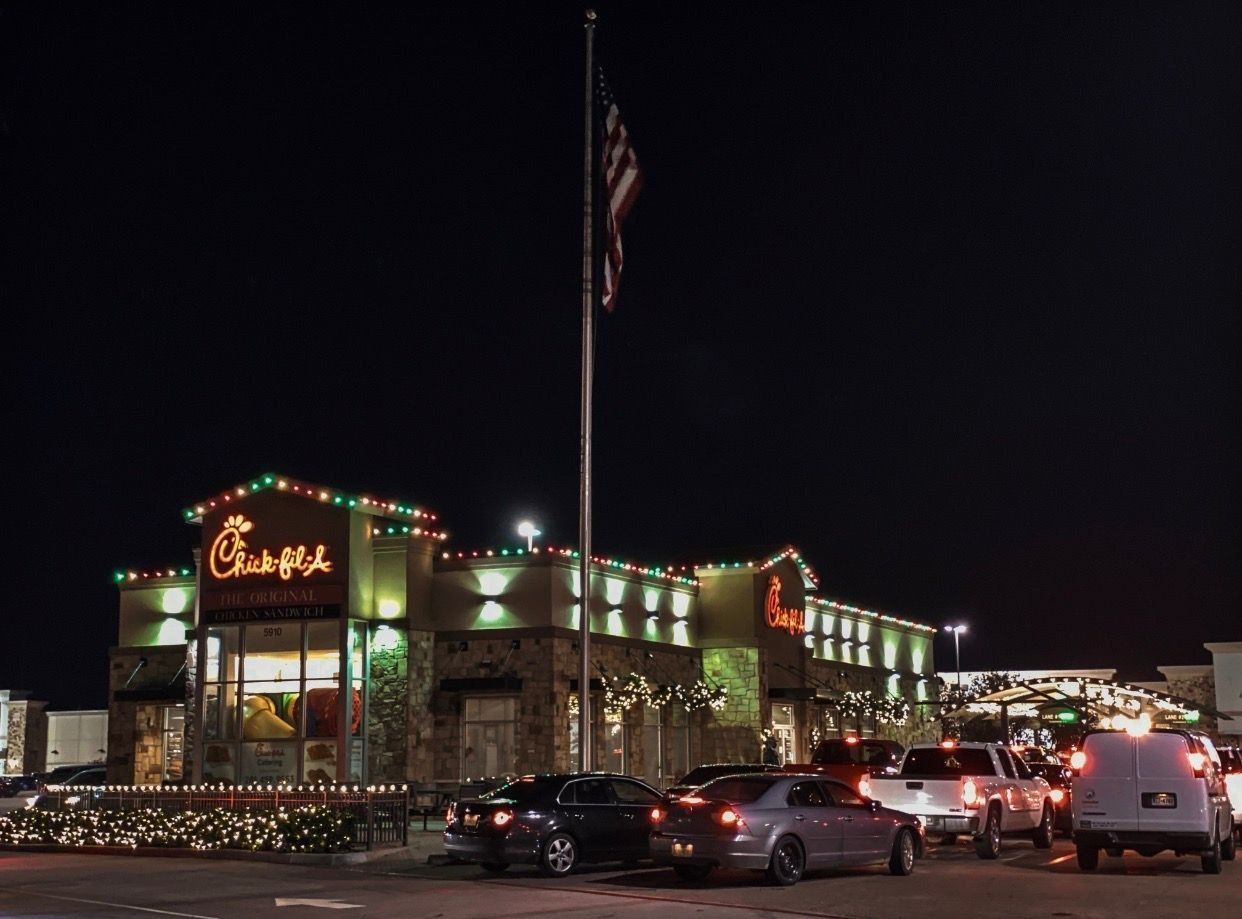 Nighttime street view of a lit restaurant with parked cars and an American flag outside