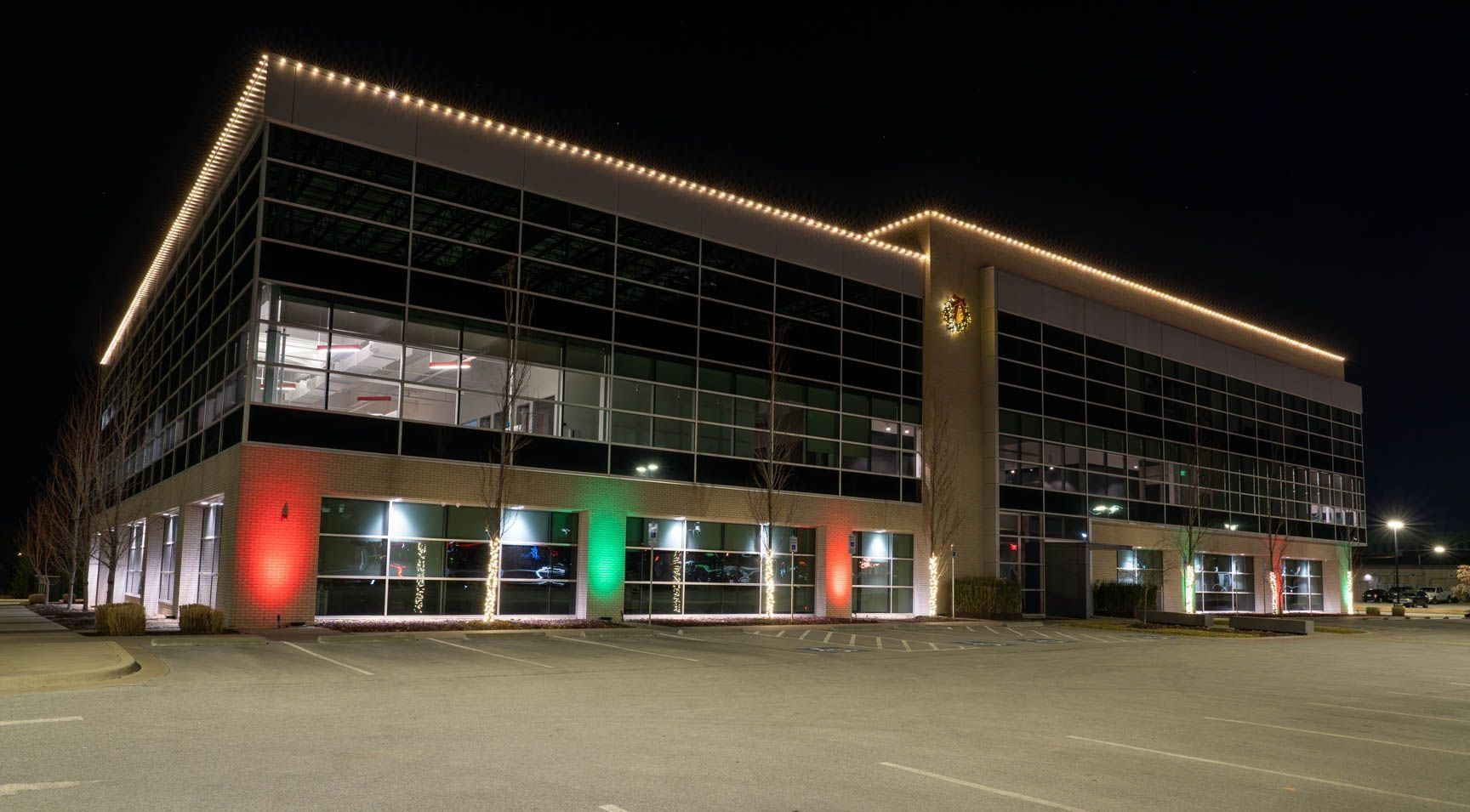 Modern glass office building at night, outlined with warm lights and red and green accent lighting.