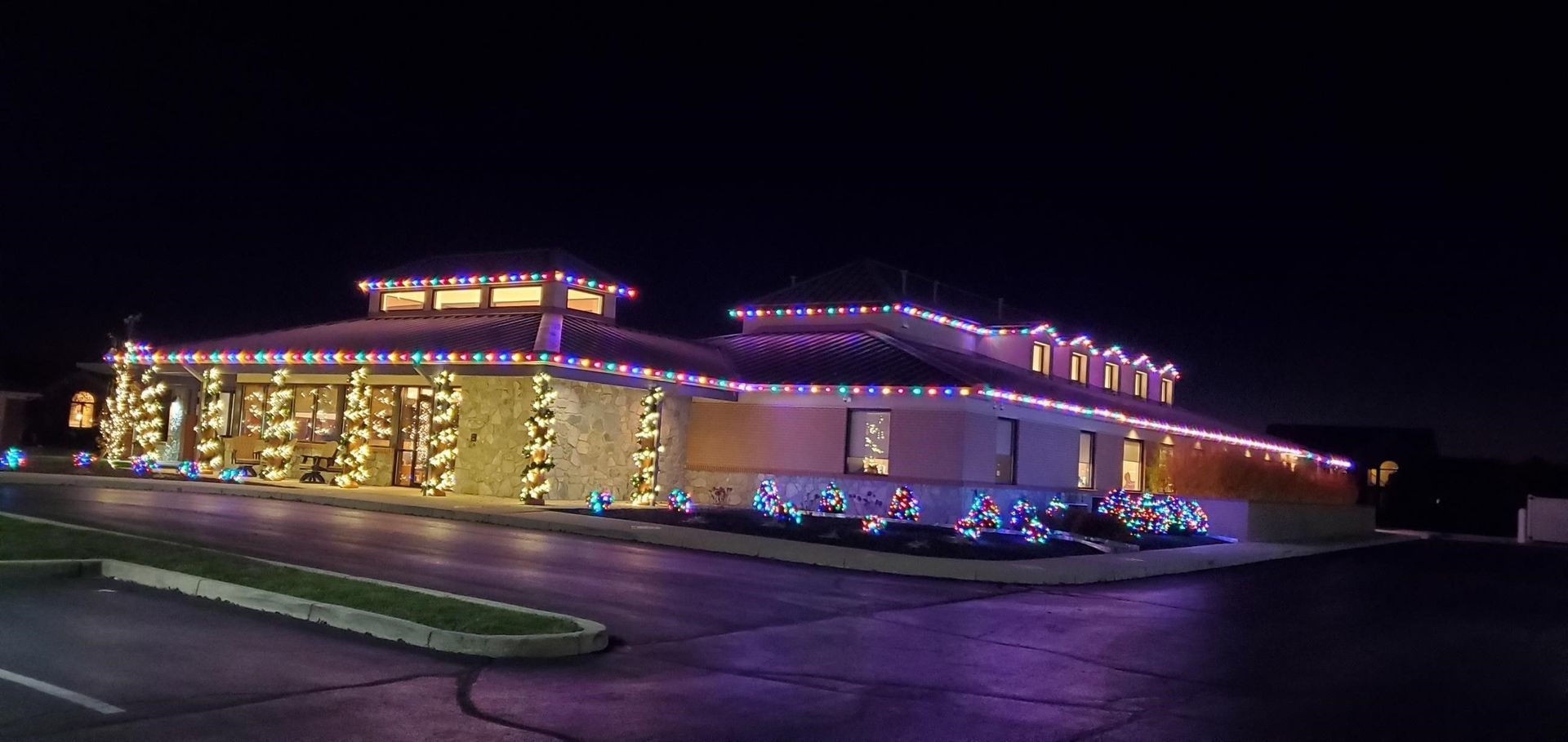 Restaurant building lit with purple and warm holiday lights at night, seen from a parking lot