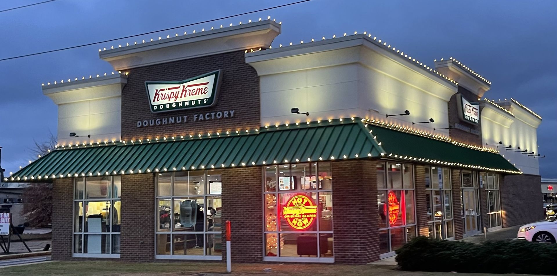 Krispy Kreme shop exterior at dusk with glowing sign and green roof