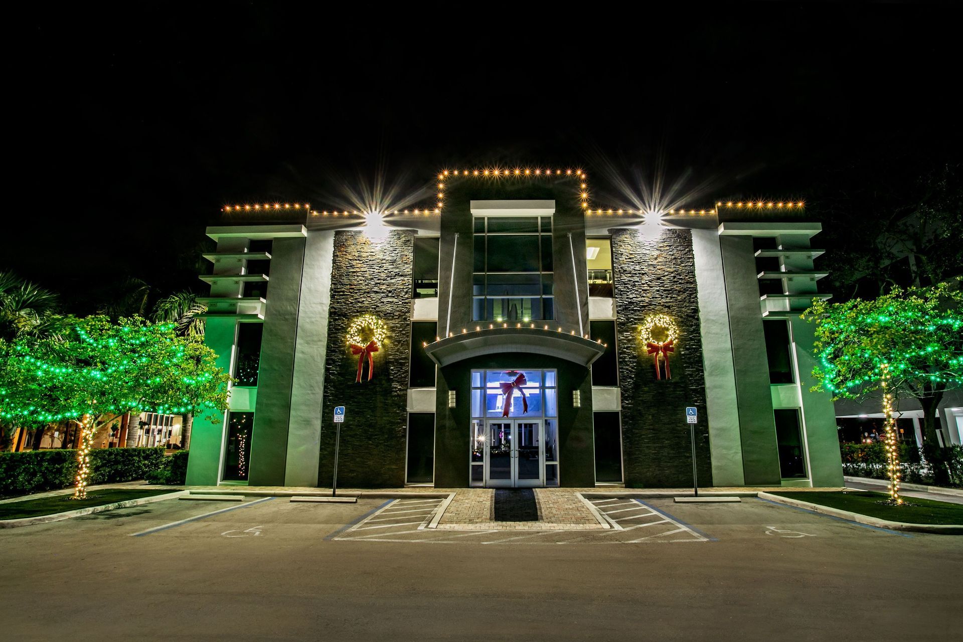 Illuminated modern building at night with green-lit trees and an empty parking lot in front