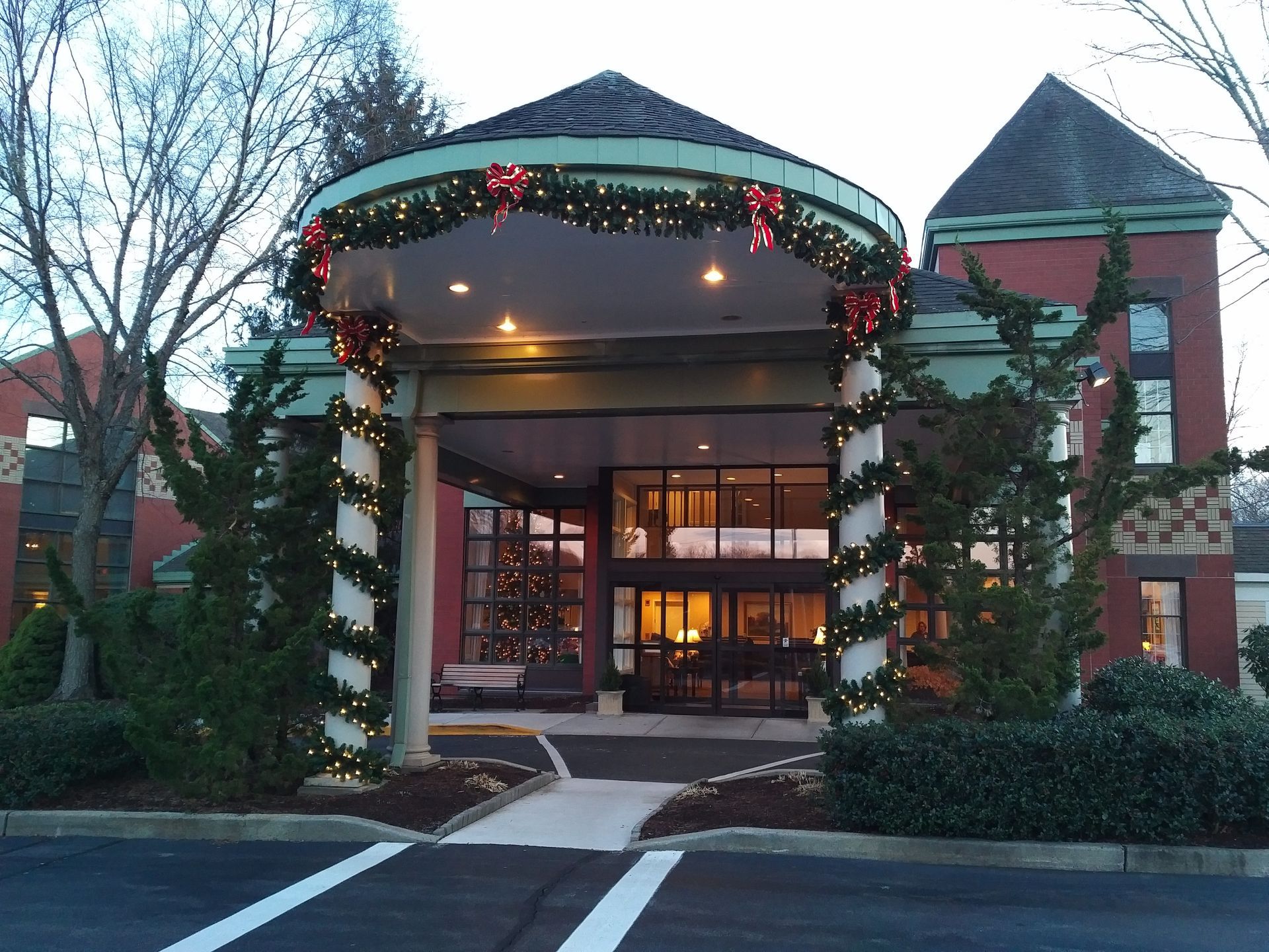 Holiday-decorated building entrance with lit canopy, wreaths, and brick towers at dusk