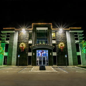 Nighttime view of a lit modern building with stone columns, green accents, and a glass entrance.
