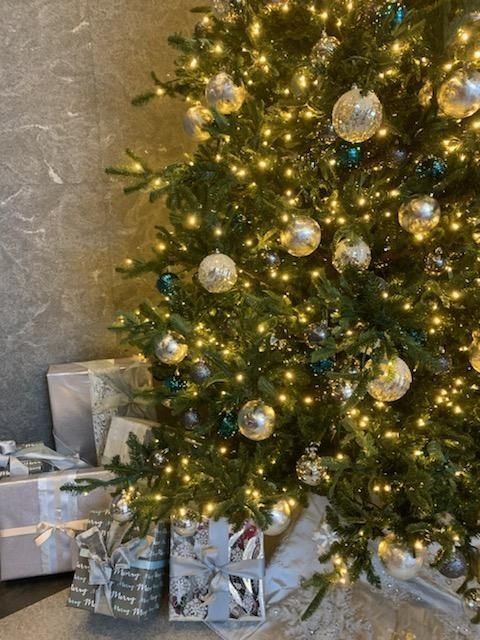Decorated Christmas tree with lights and silver ornaments beside wrapped gifts
