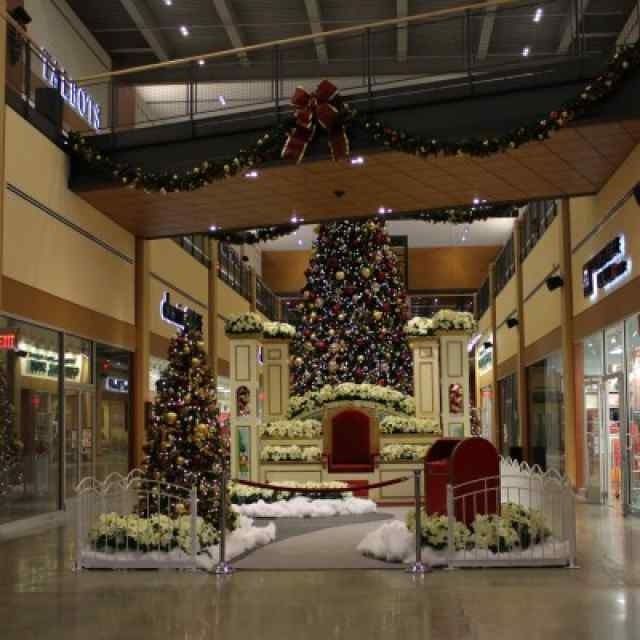 Festive holiday display with decorated Christmas trees, red chairs, and white flocking in a mall atrium