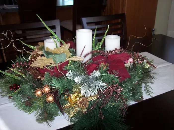 Christmas centerpiece with red flowers, candles, pine branches, and gold ornaments on a table