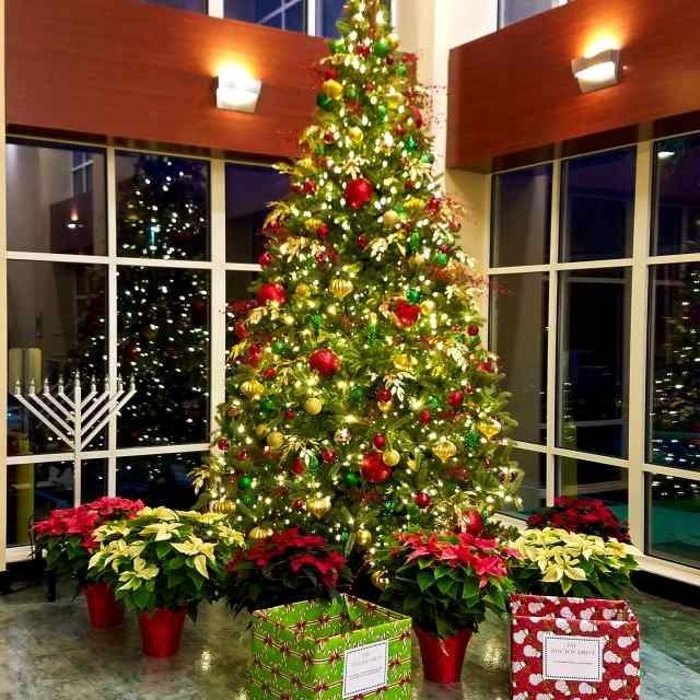 Decorated Christmas tree in a lobby with poinsettias and holiday gifts below