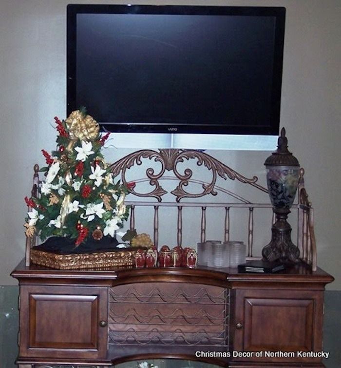 Flat-screen TV above a wooden dresser with Christmas decorations, including a small tree and candles