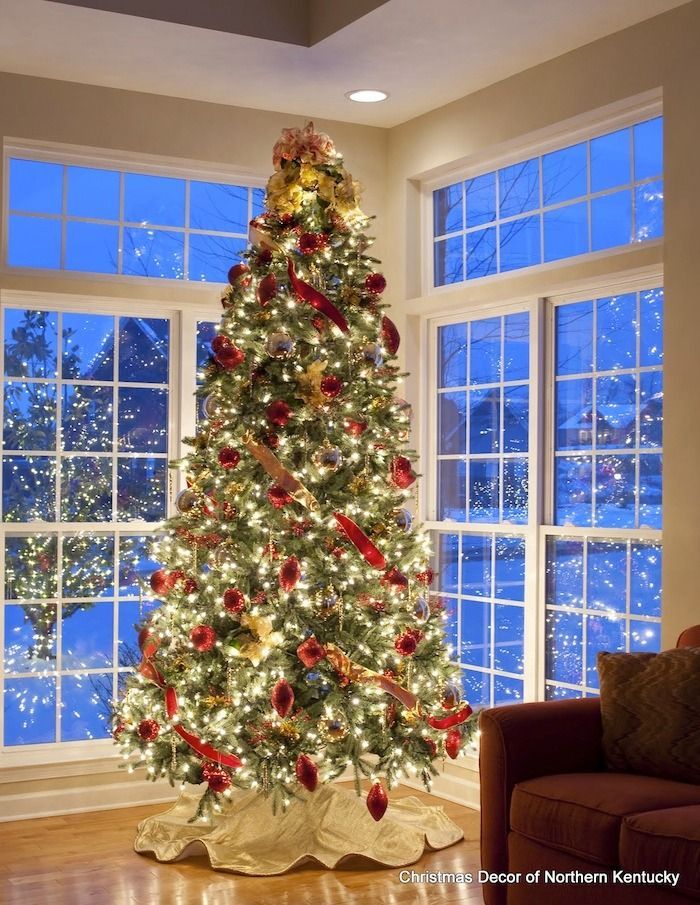 Decorated Christmas tree glowing with lights beside large windows at dusk