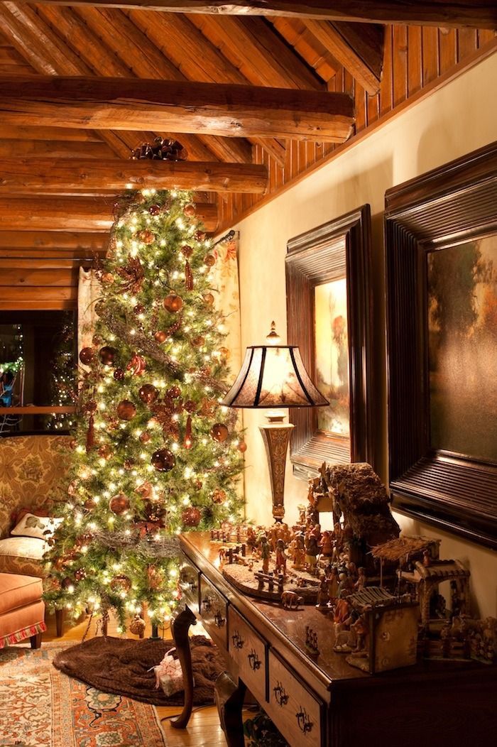 Decorated Christmas tree in a cozy living room with warm wood beams and a lit table lamp