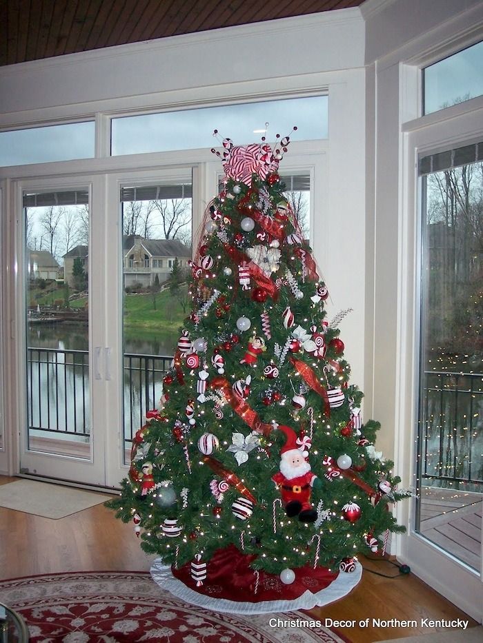 Decorated Christmas tree with red and white ornaments in a bright room by large windows