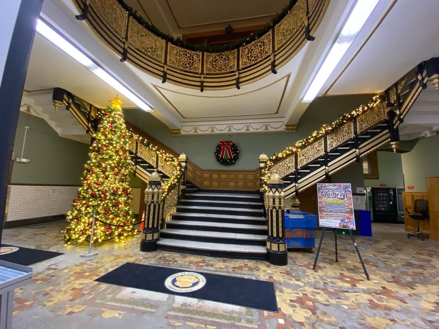 Grand lobby with twin staircases, holiday tree, and wreath under a curved balcony
