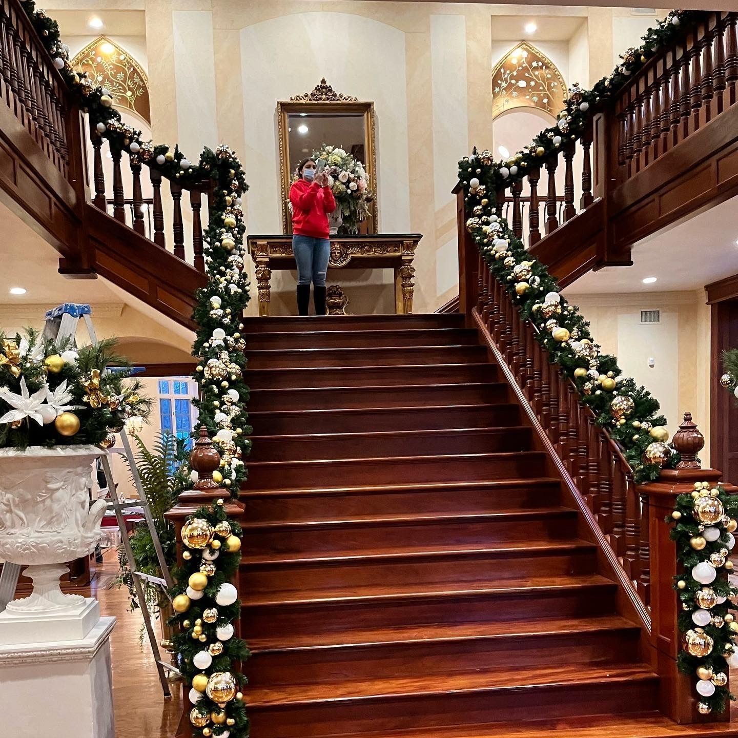 Grand staircase decorated with holiday garlands, with a person in a red jacket standing at the top.