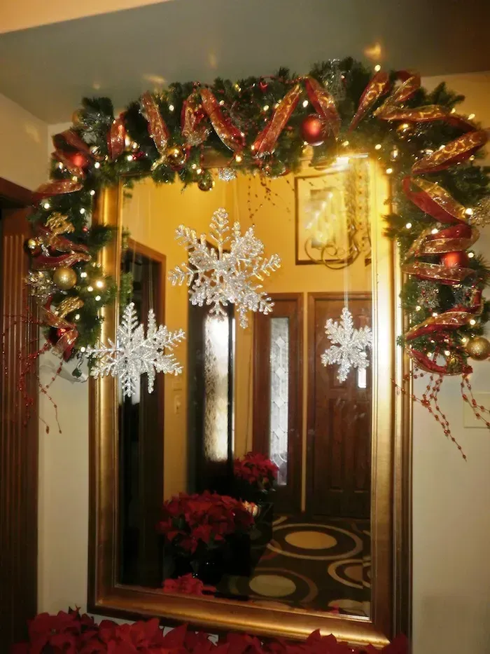 Christmas-decorated doorway with garland, lights, red bows, and hanging snowflakes