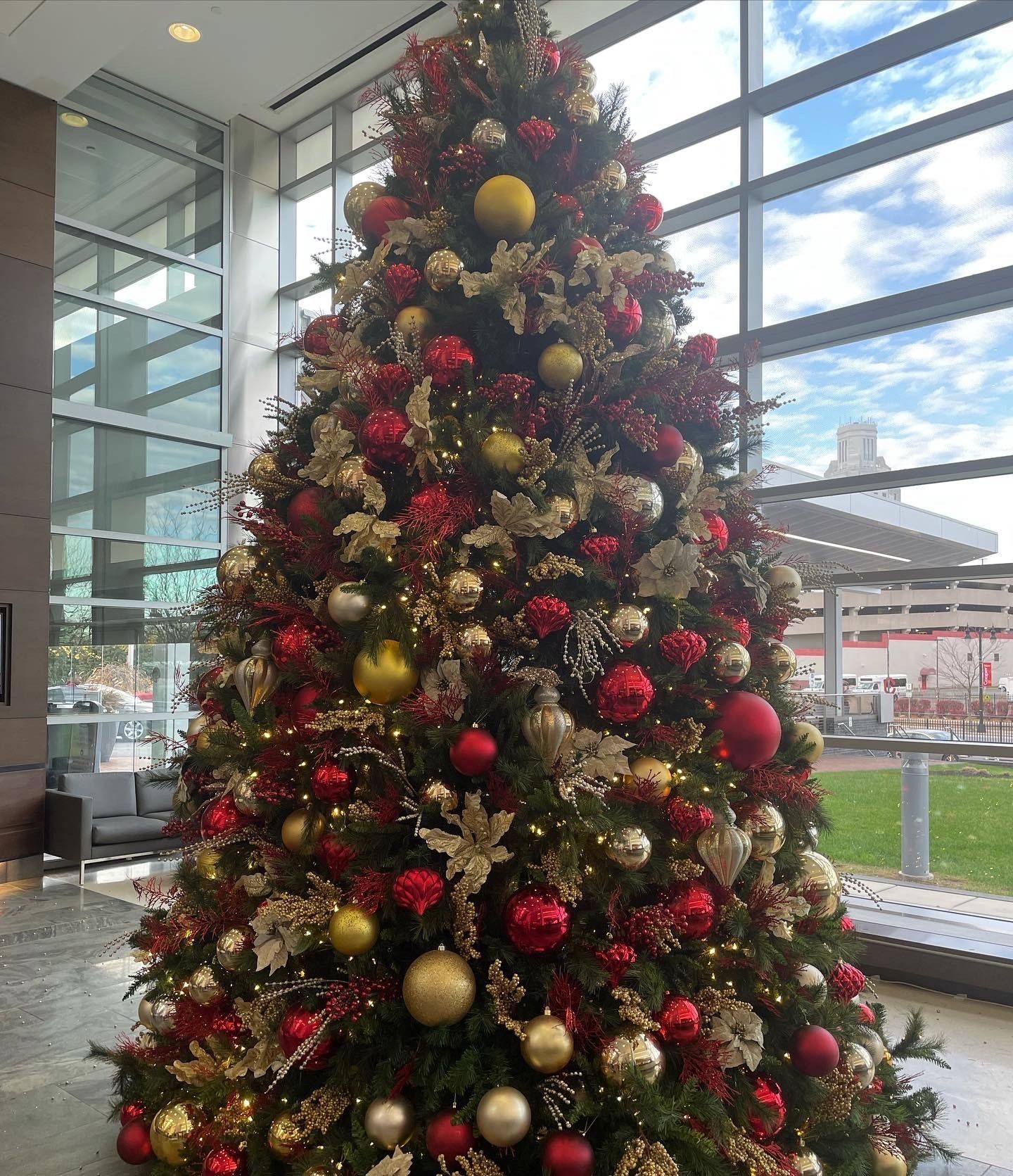 Decorated Christmas tree with red and gold ornaments in a bright glass-walled lobby