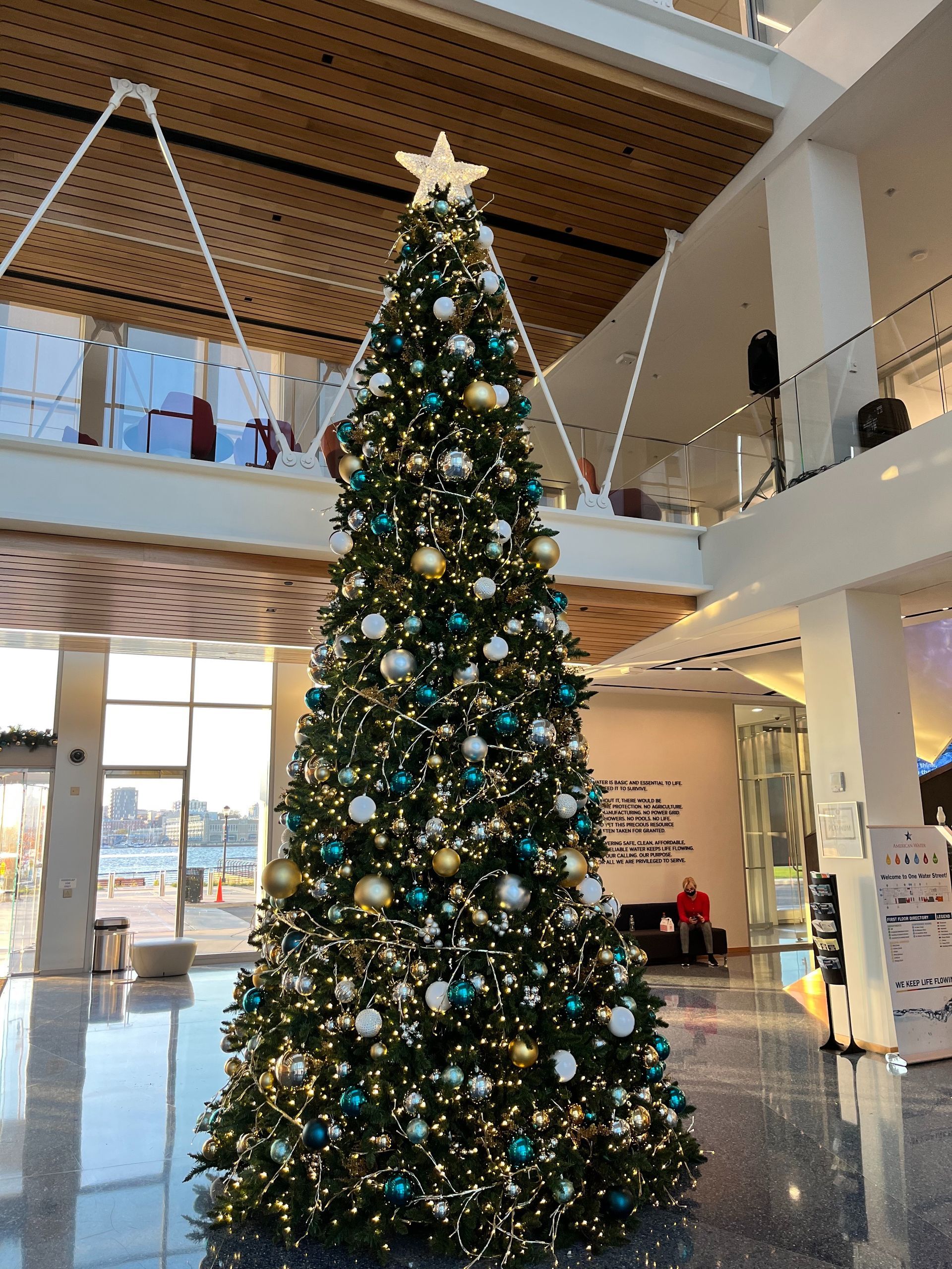 Tall decorated Christmas tree in a bright indoor atrium with blue and gold ornaments and lights