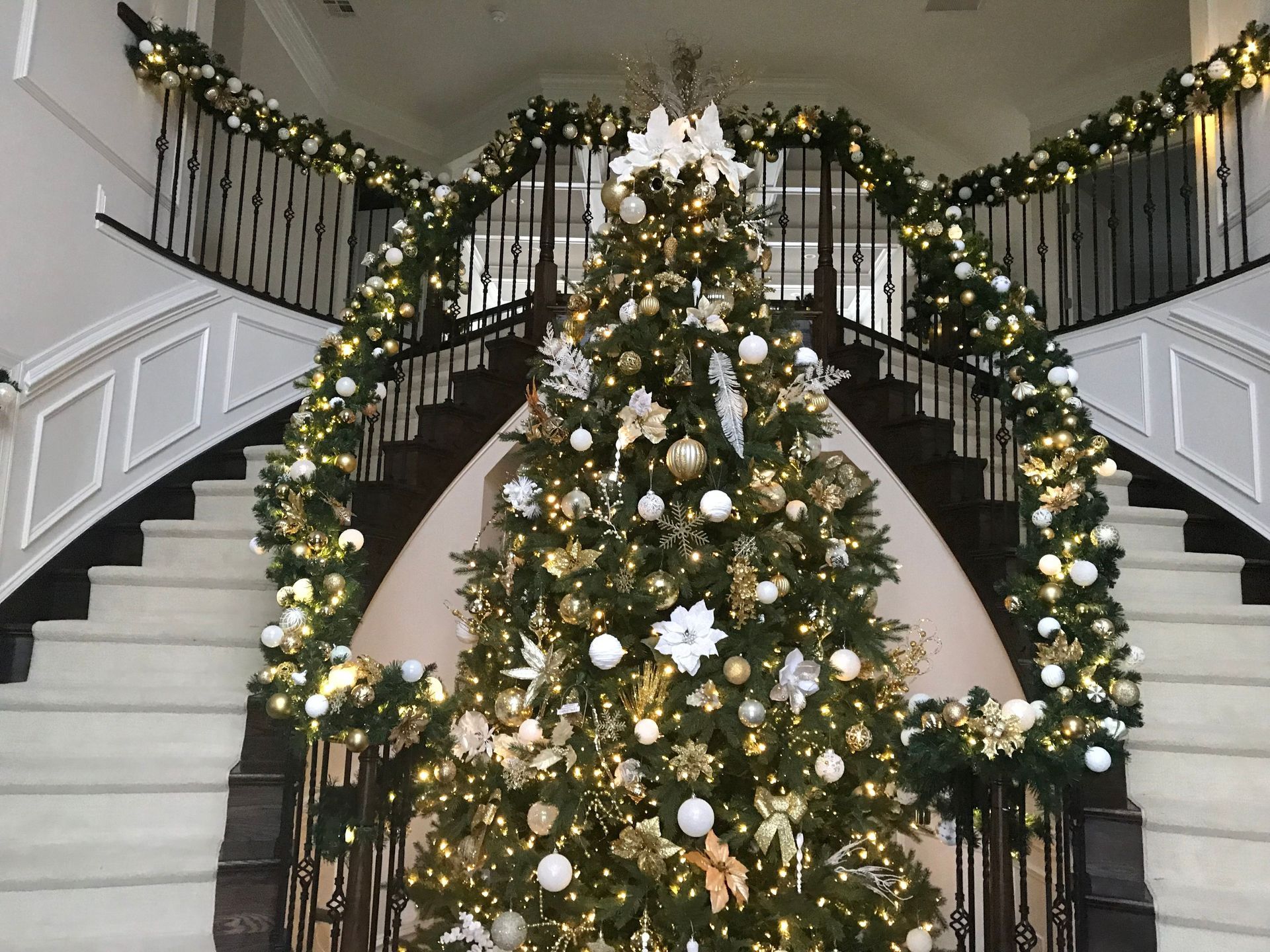 Decorated Christmas tree centered in a grand staircase lobby with garland and white ornaments