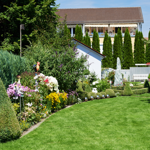 Lush garden with colorful flowers, green lawn, and a house in the background