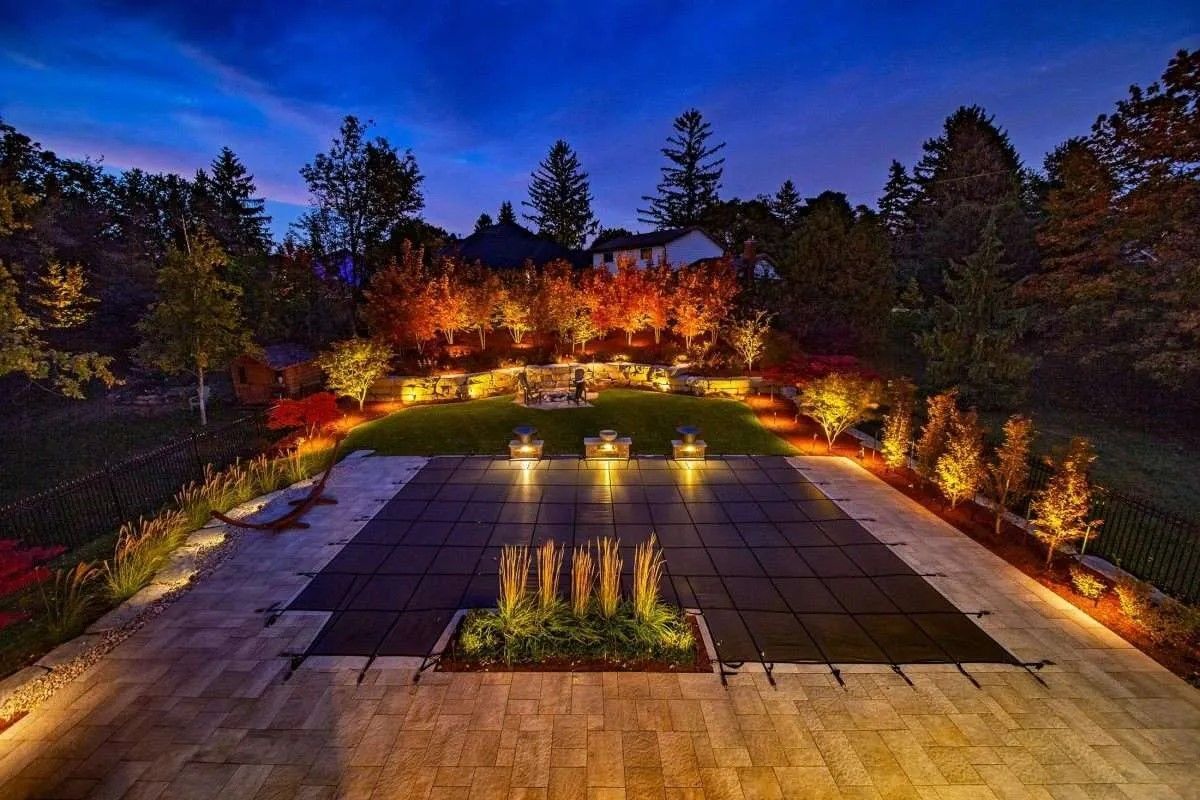 Illuminated landscaped patio with central water feature at dusk, surrounded by trees and warm lights