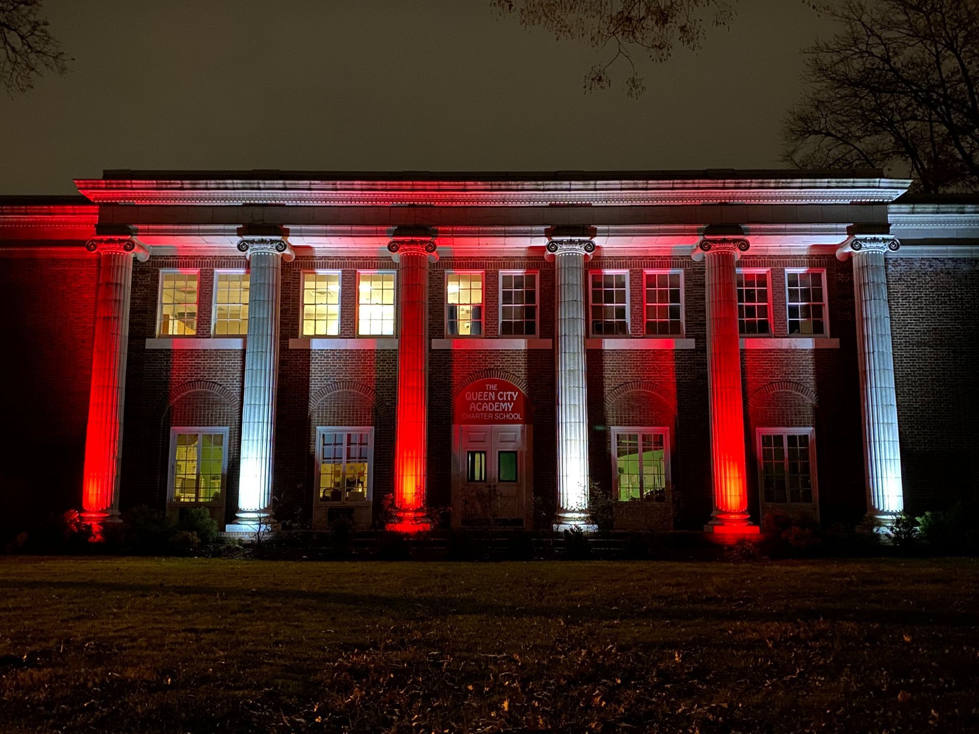 Building facade lit red and white at night, with columns and illuminated windows.