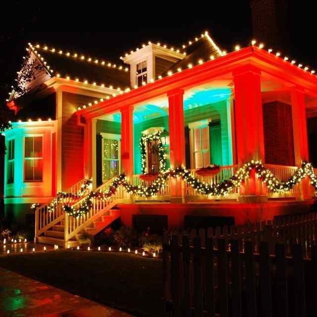 Festively lit house with red and green holiday lights and garland on the porch at night